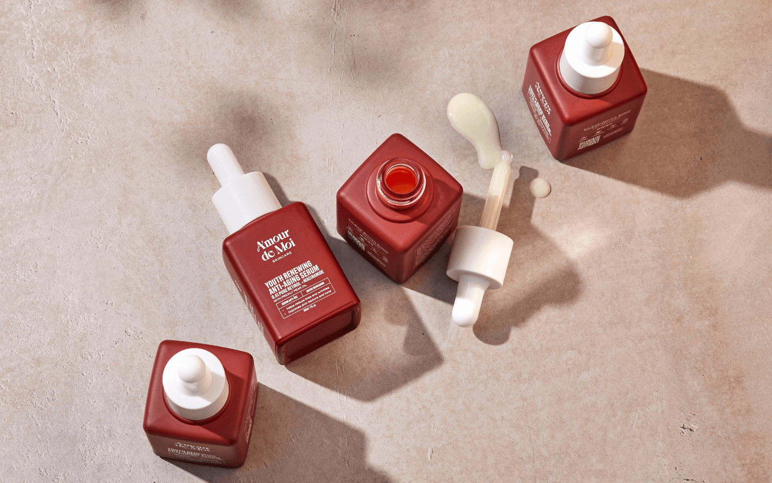 four bottles of anti-aging retinol niacinamide youth preserving serum sitting on a beige counter with shadows