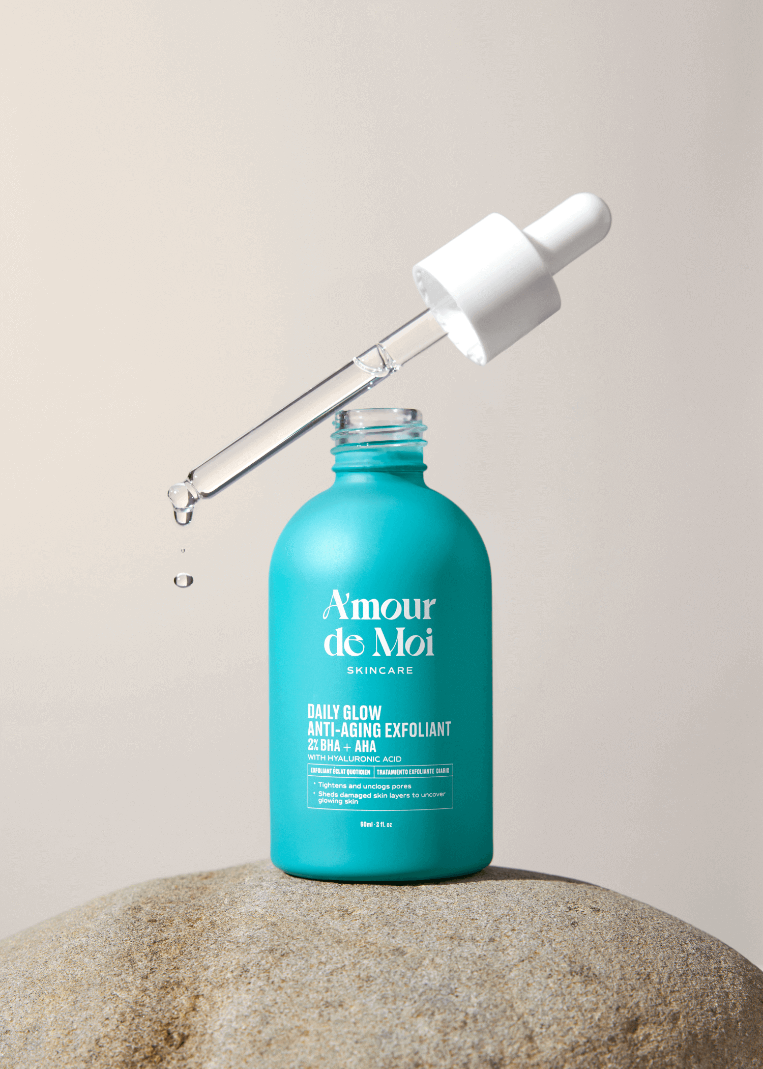 An open bottle of BHA AHA daily glow anti-aging exfoliant with dropper dripping product sitting on a rock
