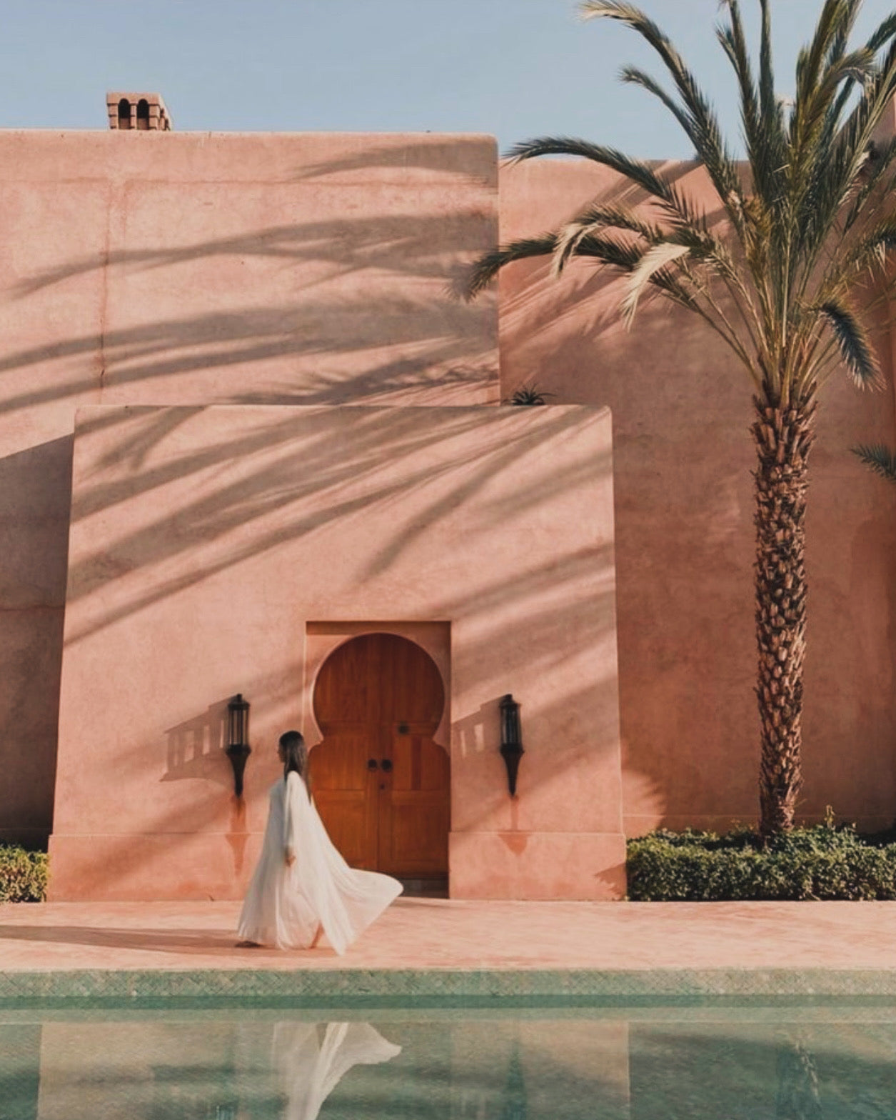 Pink Moroccan building with palm tree and woman walking in white