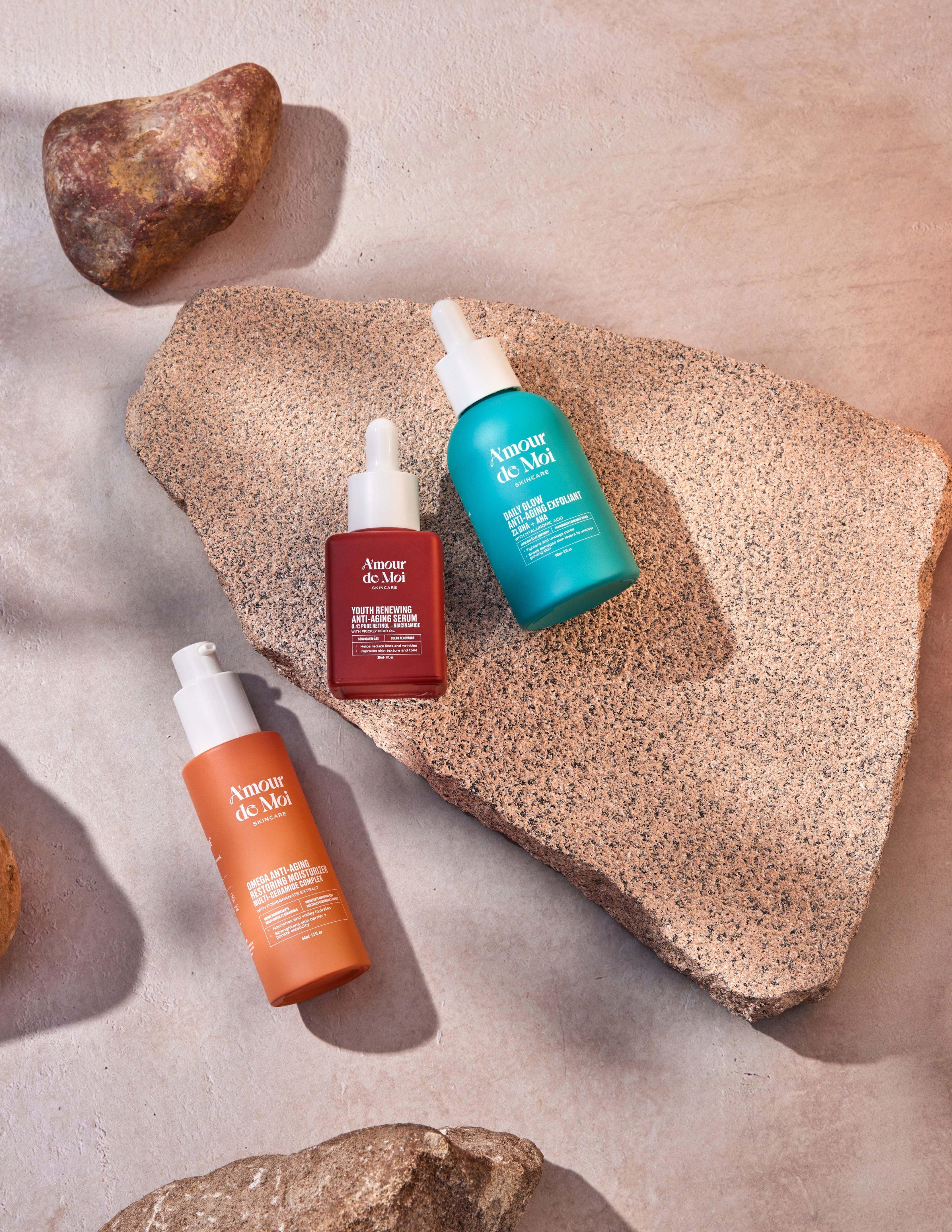 All three amour de moi anti-aging skincare products laying on rocks being showcase