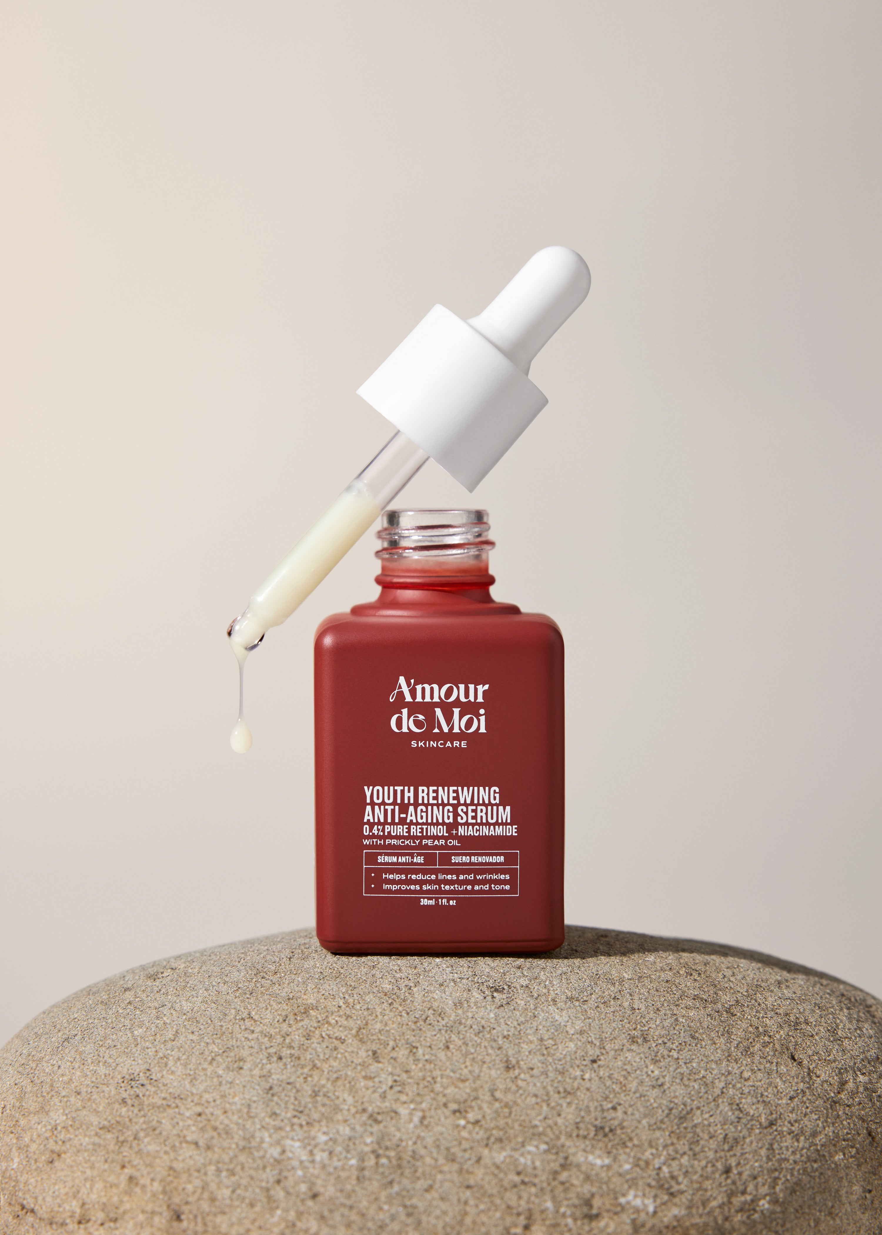 An open bottle of youth renewing anti-aging serum with dropper dripping product sitting on a rock