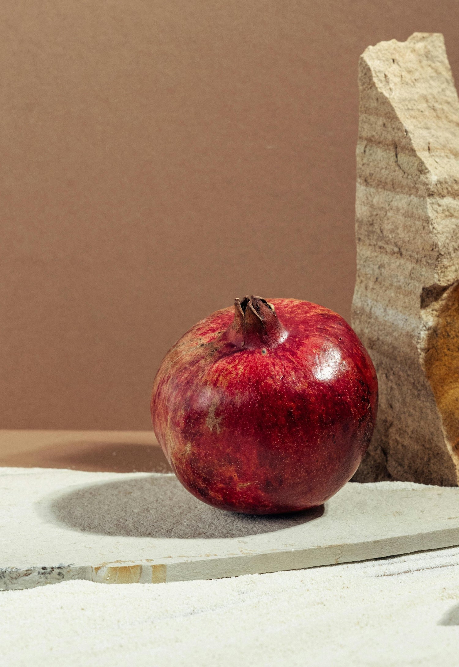 a whole red pomegranate used as a natural ingredient for skincare sitting on rocks against beige wall