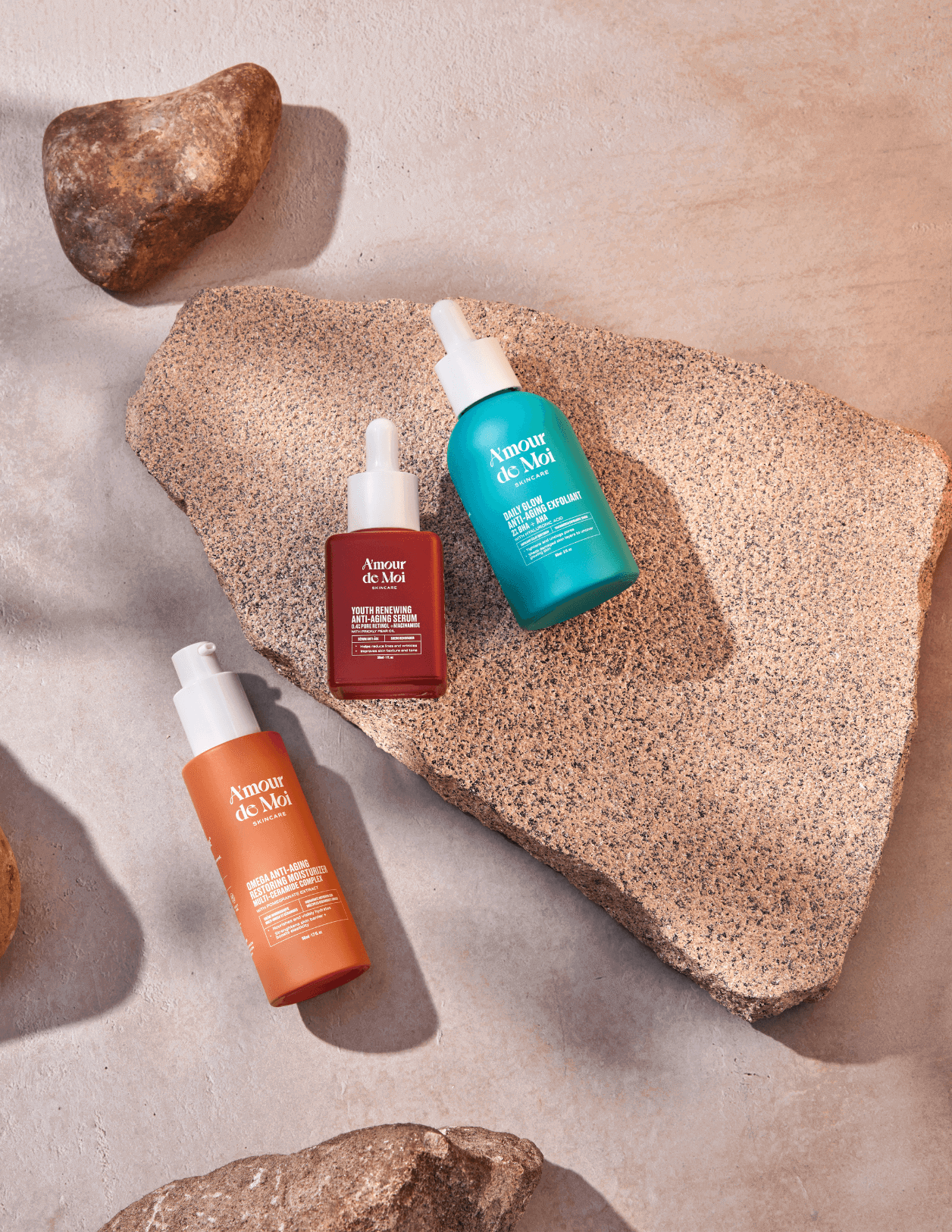 All three amour de moi anti-aging skincare products laying on rocks being showcase
