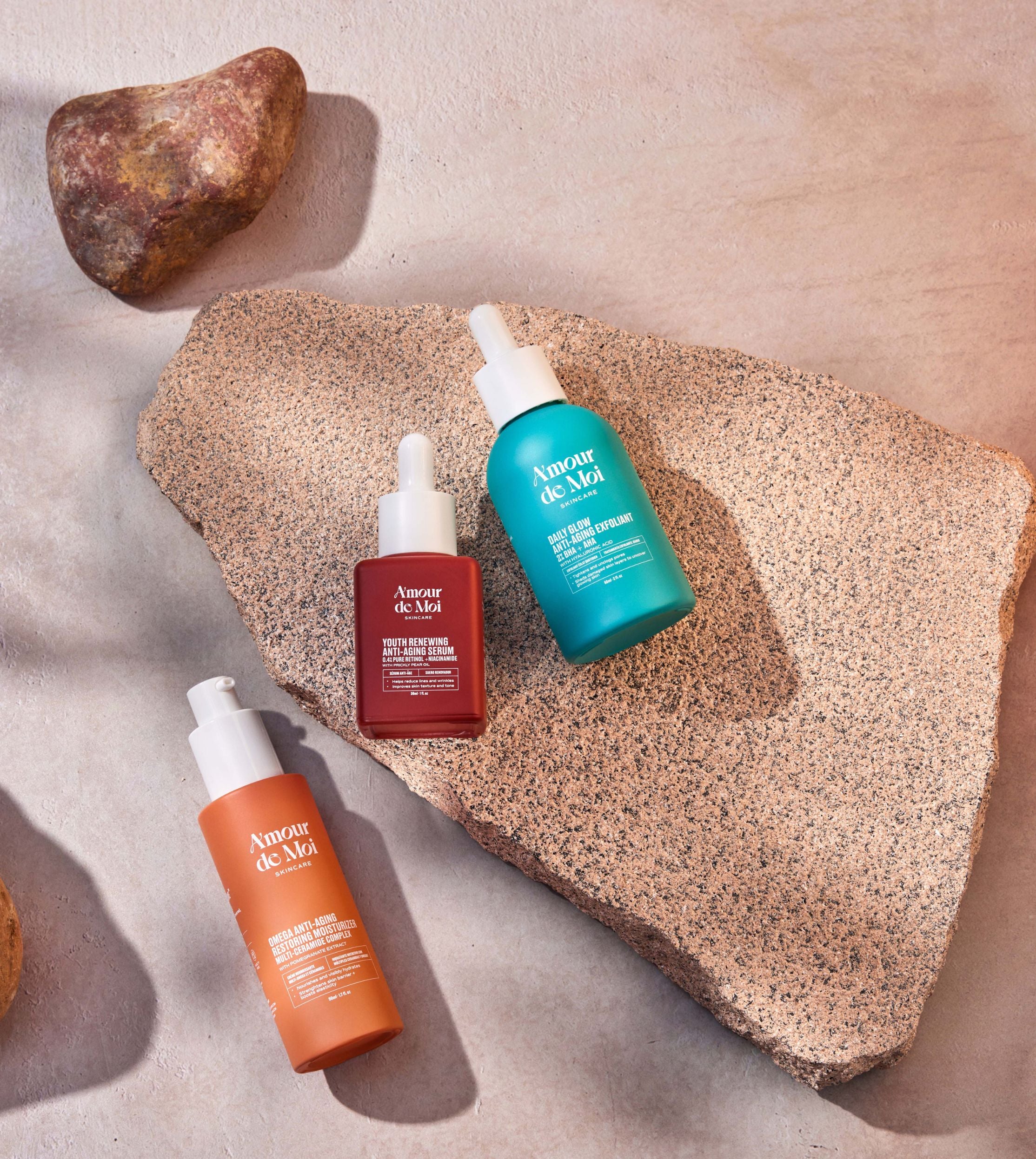 All three amour de moi anti-aging skincare products laying on rocks being showcased