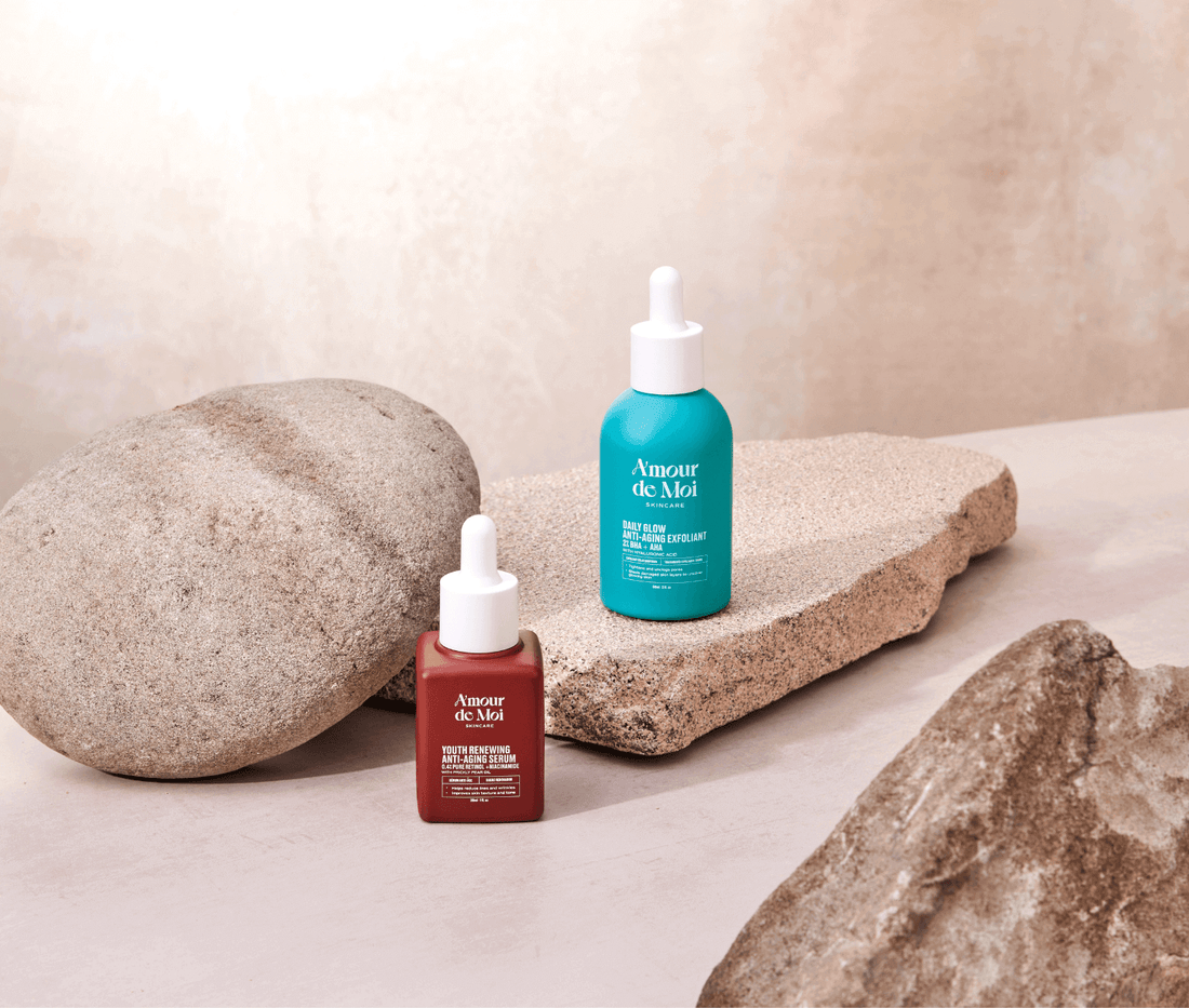 a bottle of the youth renewing anti-aging serum and the BHA AHA daily glow anti-aging exfoliant sitting on rocks