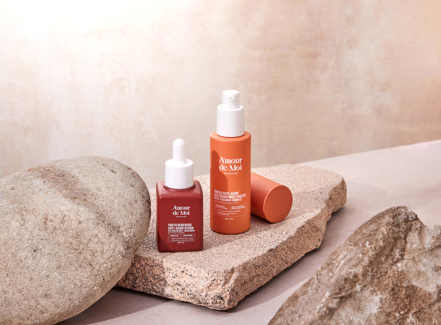 a bottle of the youth renewing anti-aging serum and the omega anti-aging restoring moisturizer multi-ceramide complex sitting on rocks