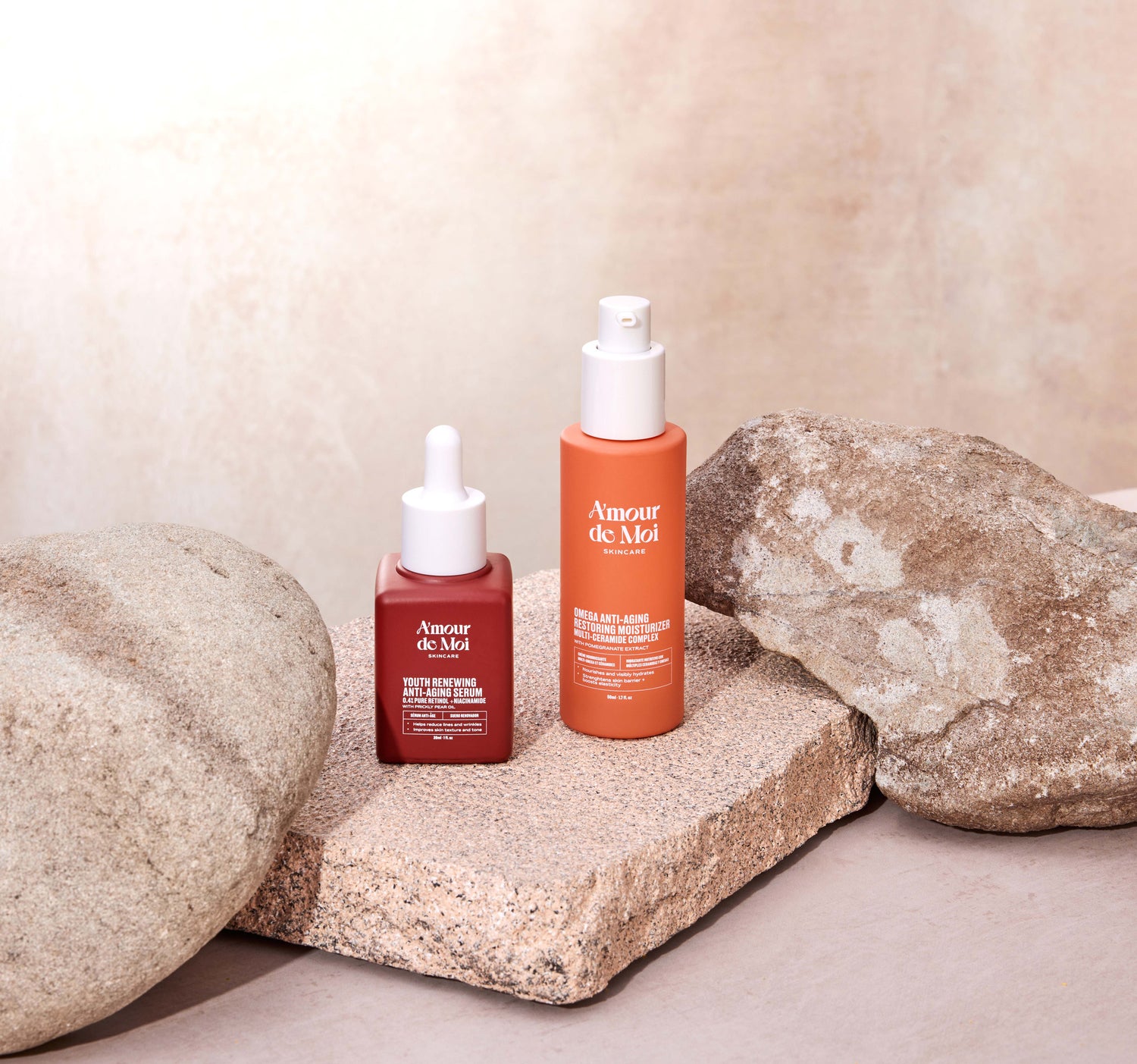 a bottle of the youth renewing anti-aging serum and the omega anti-aging restoring moisturizer multi-ceramide complex sitting on rocks